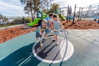 Kids playing on roundabout play equipment at a park with lake in the background